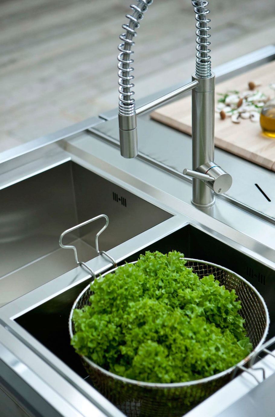 Edelstahl-Küchenspüle mit flexiblem Wasserhahn und grünem Salat im Abtropfsieb