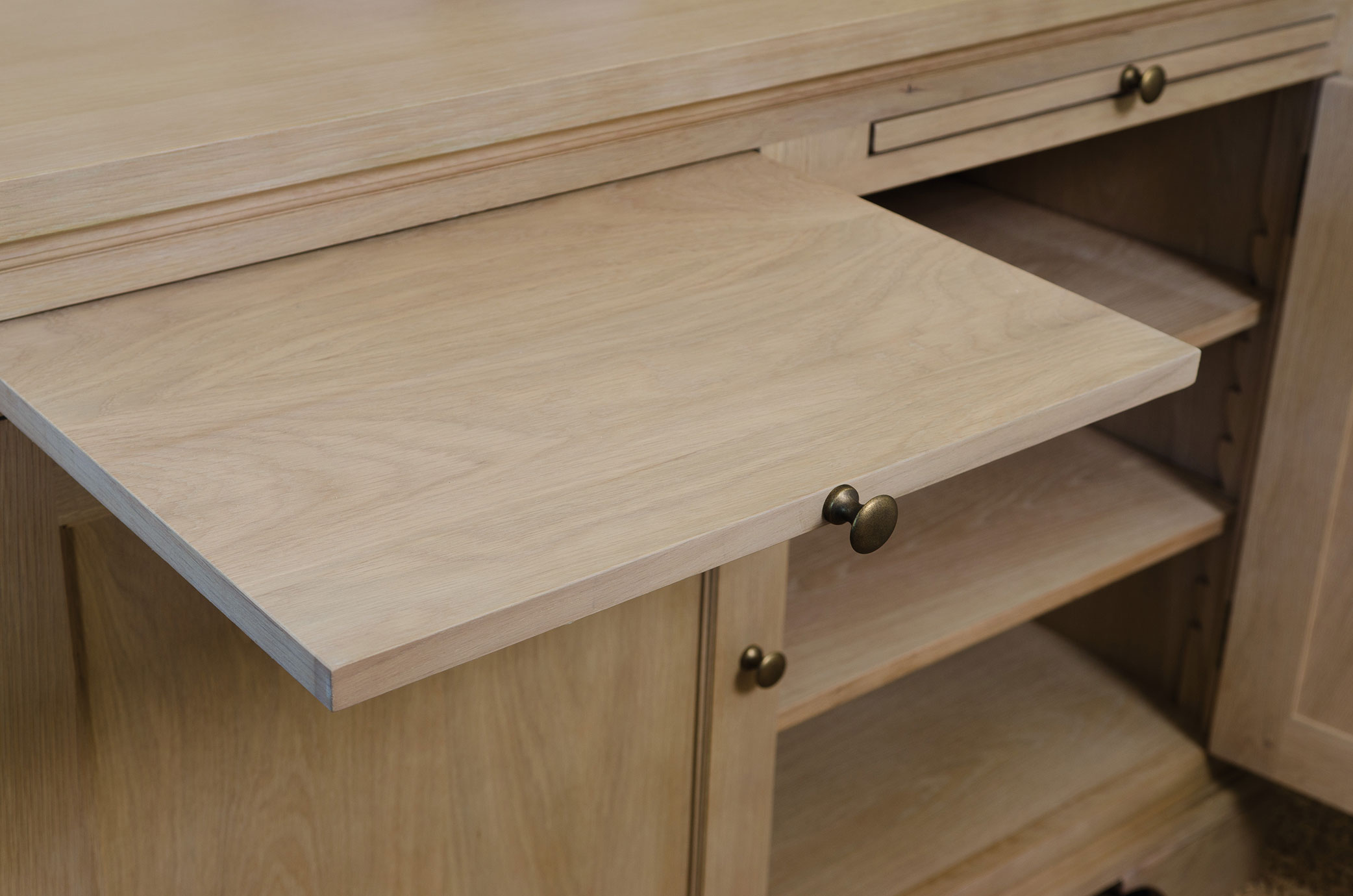 Detailansicht eines ausziehbaren Ablagebodens mit Messingknopf an einem Sideboard aus hellem Massivholz