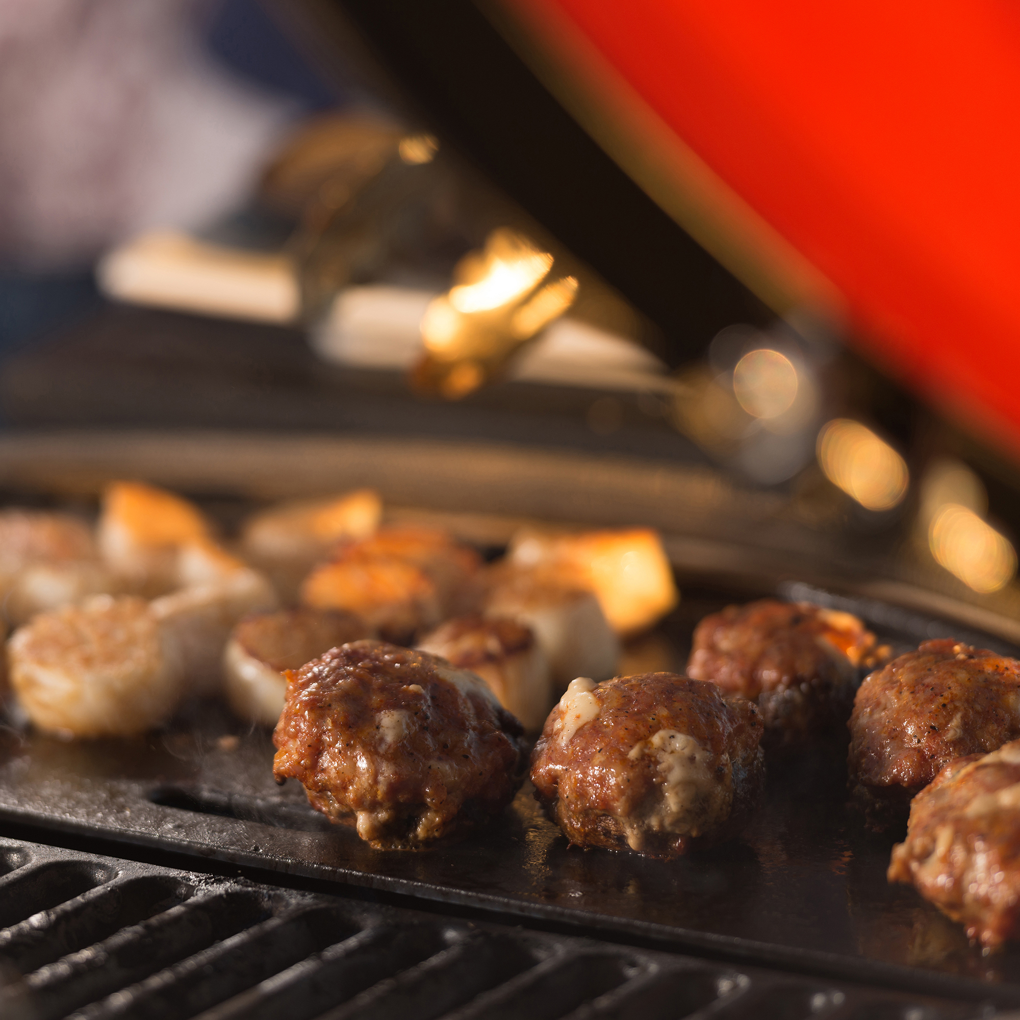 Saftige Fleischbällchen und Meeresfrüchte werden auf einem Grill zubereitet, der Deckel ist geöffnet.