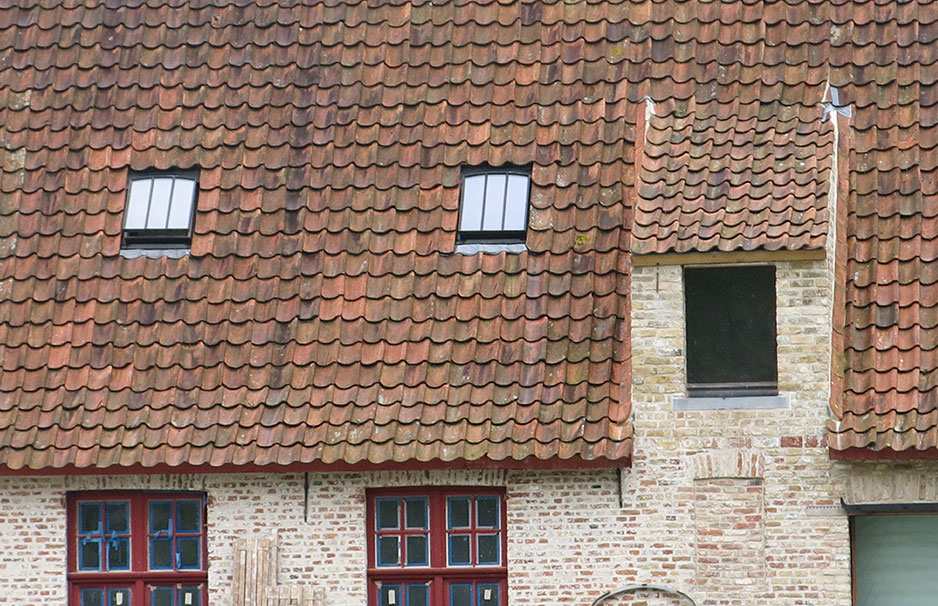 Historisches Gebäude mit roten Dachziegeln, zwei kleinen Fenstern im Dach und einer offenen Fensterluke
