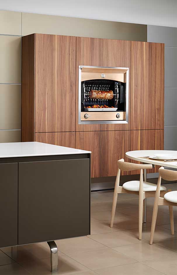 Moderner Einbau-Grillofen mit Drehspieß und Grillgut, integriert in elegante Holzküche neben Esstisch