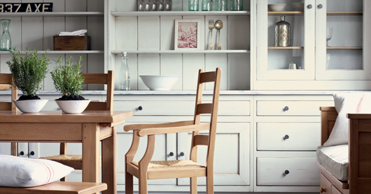 Ein heller Essbereich im Landhausstil mit Holztisch, Holzstühlen, Bank mit Kissen und weißem Geschirrschrank