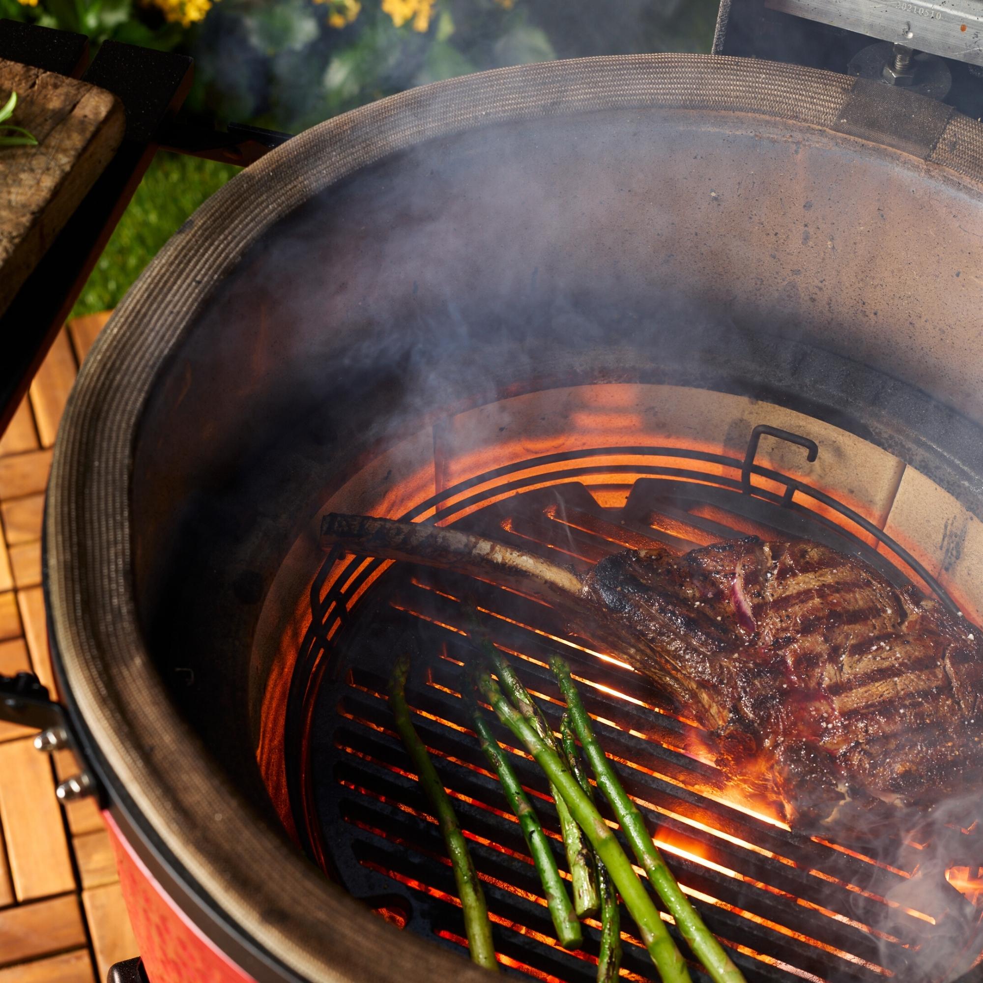 Ein Tomahawk-Steak und mehrere grüne Spargelstangen werden auf einem Grill bei starker Hitze und offener Flamme gegrillt
