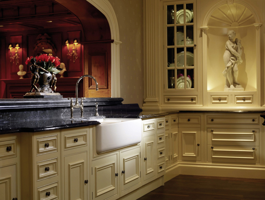 Elegante Küche im klassischen Stil mit cremefarbenen Holzmöbeln, schwarzer Marmorarbeitsplatte, nostalgischem Spülbecken und eingebauter Statue