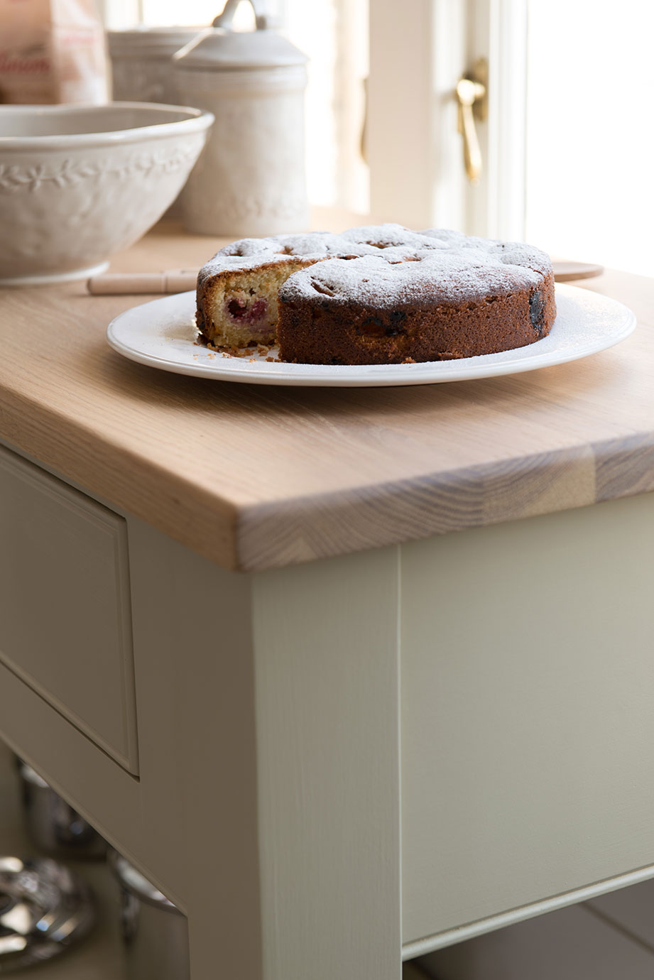 Hausgemachter Kuchen mit Kirschen und Puderzucker bestäubt, serviert auf einem weißen Teller auf einer hellen Küchenarbeitsplatte