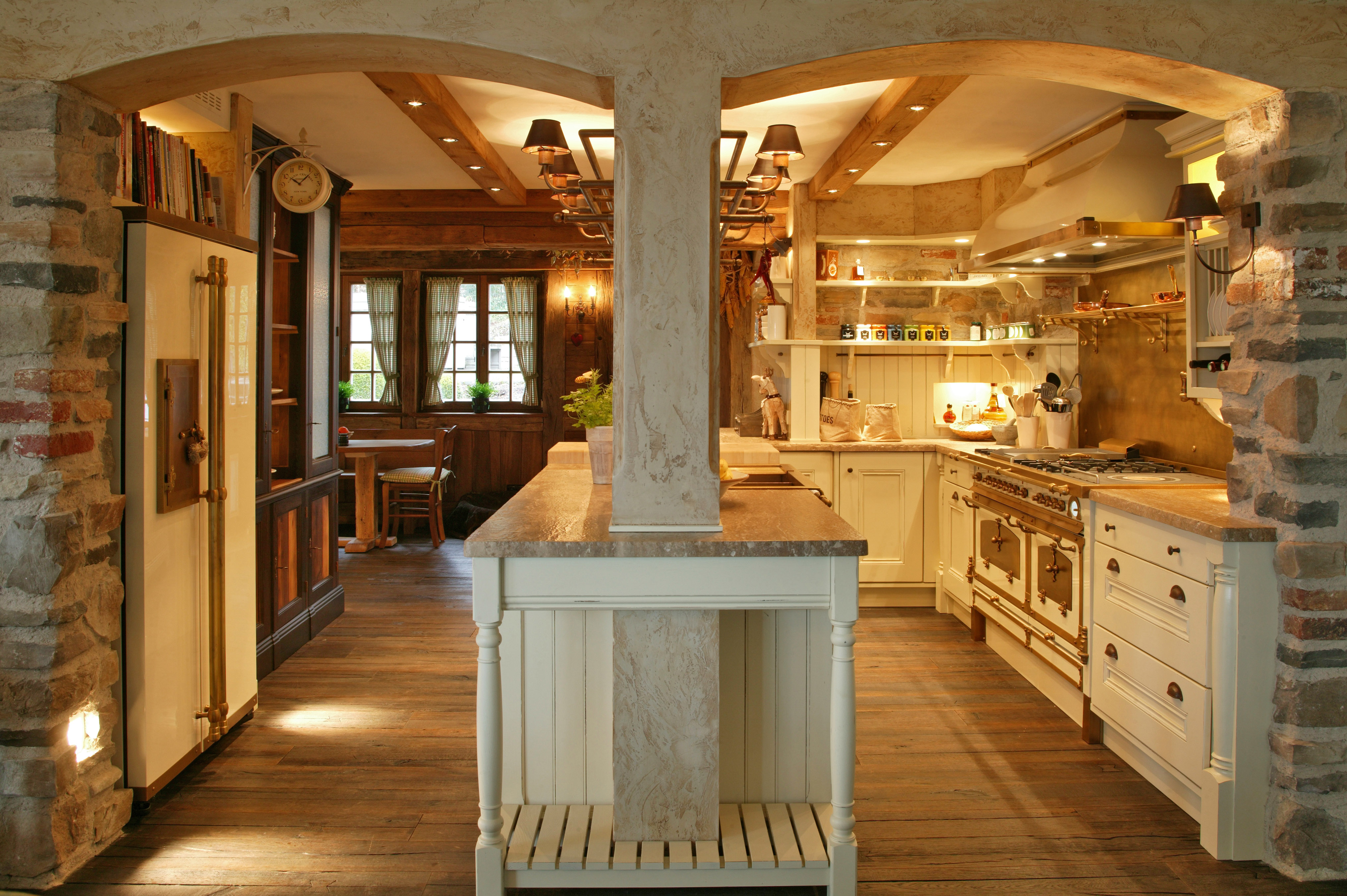 Gemütliche Landhausküche mit Holzboden, cremefarbenen Möbeln, Natursteinwänden und stilvoller Beleuchtung im rustikalen Design