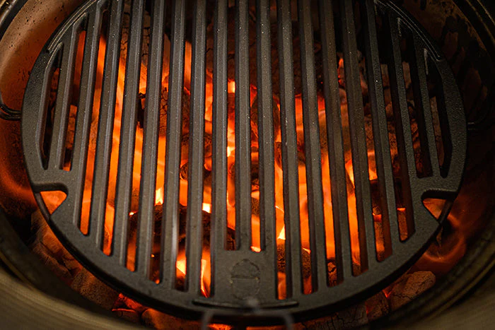 Runder gusseiserner Grillrost auf einem Grill mit brennender Holzkohle und sichtbaren Flammen