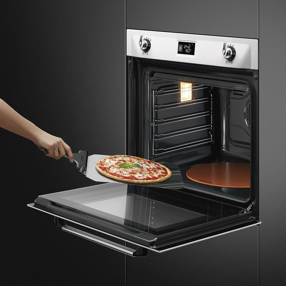 Hand nimmt mit Pizzaschaufel eine frisch gebackene Pizza aus einem modernen Einbau-Backofen mit eingeschaltetem Licht heraus