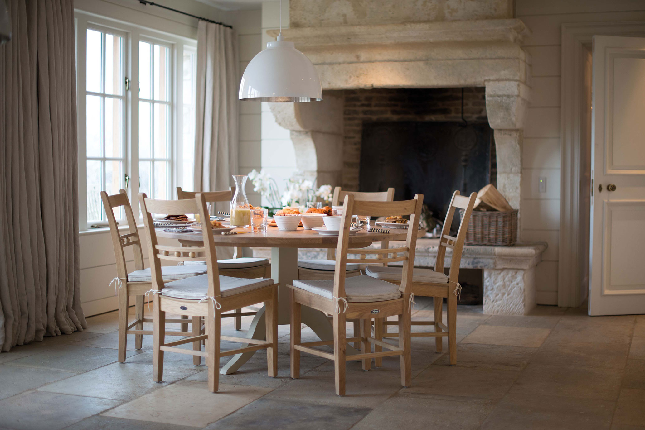 Gemütlich eingerichtetes Esszimmer mit rundem Holztisch, sechs Holzstühlen, großer Steinkamin und liebevoll gedecktem Frühstückstisch in heller, freundlicher Atmosphäre