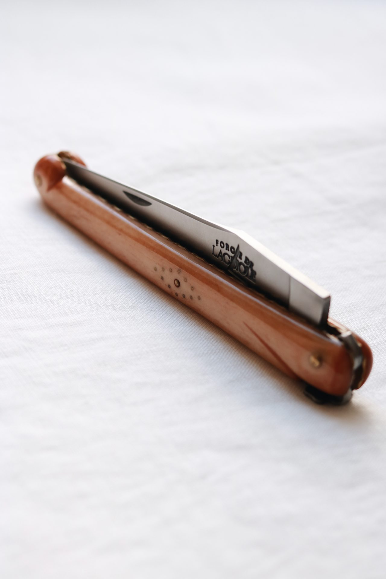 Zusammengeklapptes Taschenmesser mit Holzgriff und sichtbarer Edelstahlklinge auf weißem Stoff