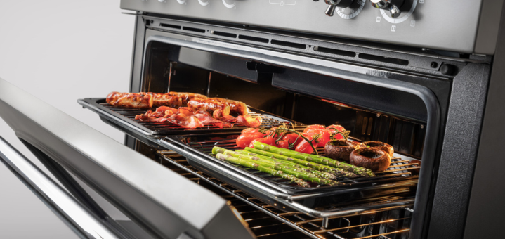 Geöffneter Backofen mit gegrilltem Spargel, Tomaten, Champignons, Speck und Fleisch auf Backblechen