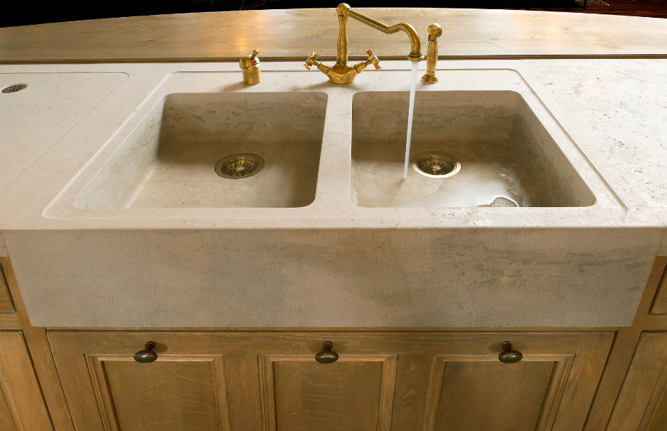 Massives Doppelspülbecken aus Stein mit goldfarbener Wasserarmatur auf einer Holzunterschrank-Küche, Wasser läuft aus dem Wasserhahn.