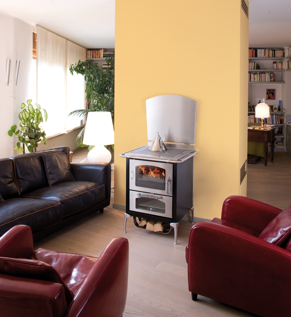 Modern eingerichtetes Wohnzimmer mit schwarzem Holzofen, zwei roten und einem schwarzen Ledersofa, gelber Wand und viel Tageslicht