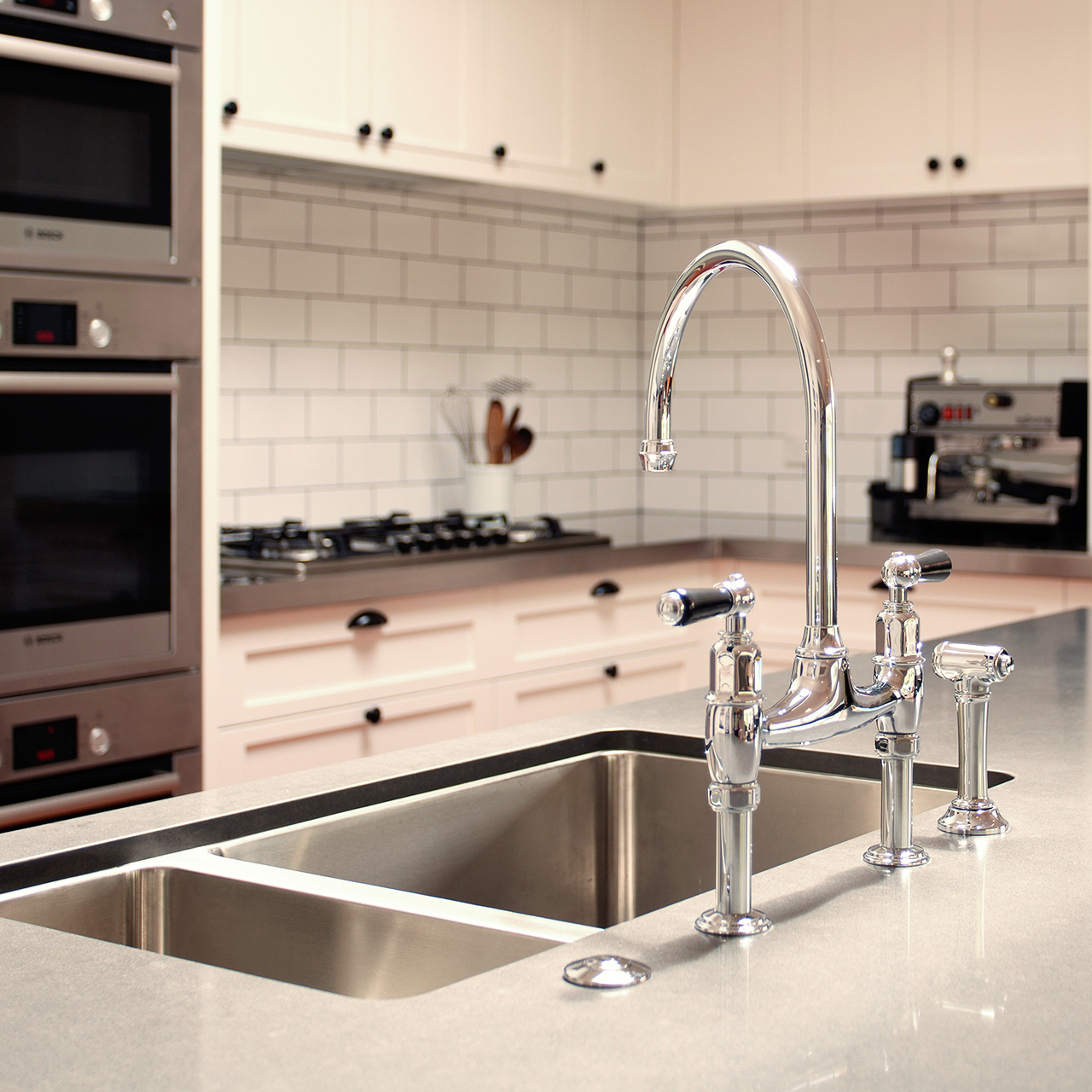 Zweifach-Edelstahlspüle mit glänzendem Wasserhahn auf Küchenarbeitsplatte, im Hintergrund weiße Küchenschränke, Herd und Kaffeemaschine