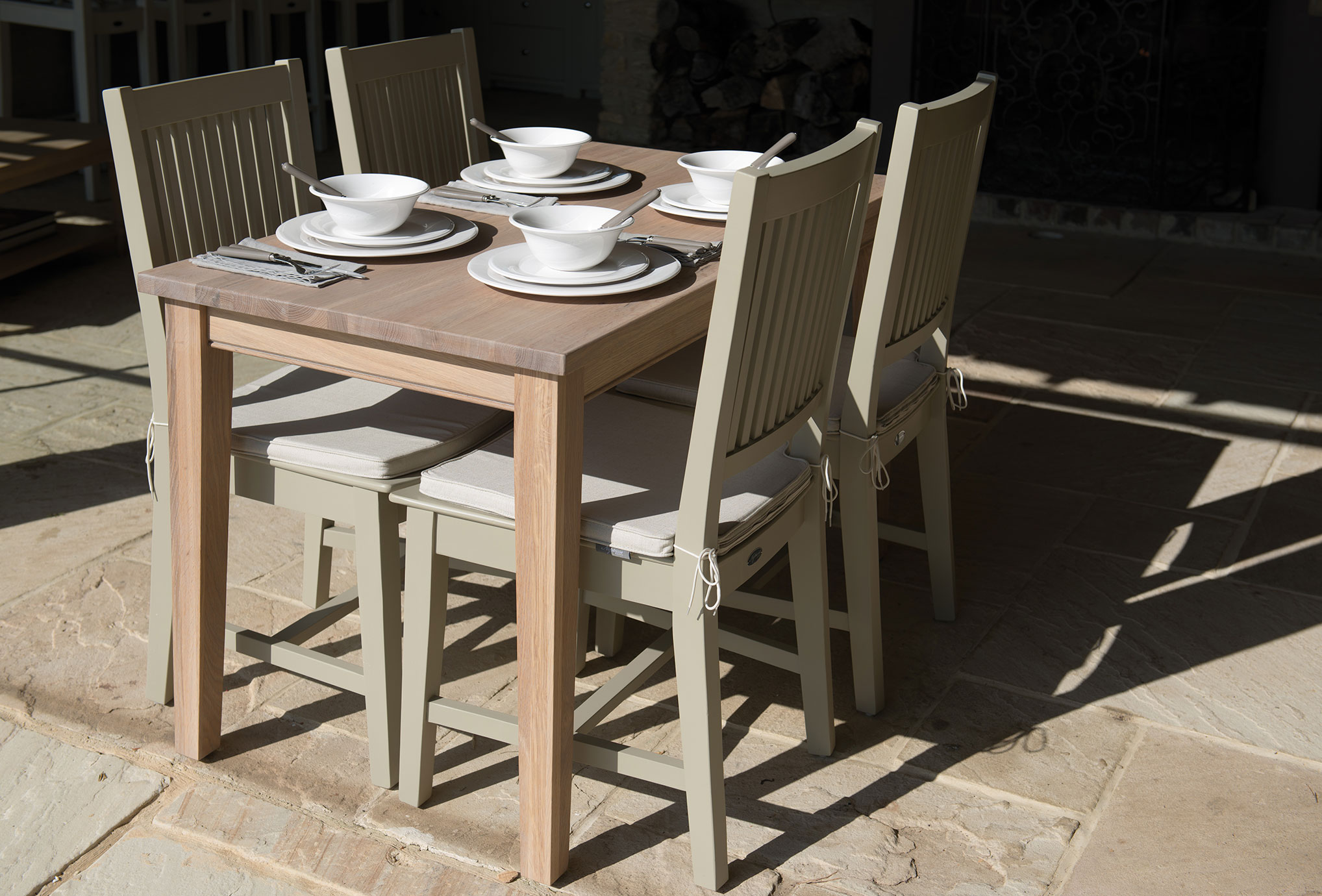 Moderner Esstisch aus Holz mit vier hellen Stühlen, weißem Geschirr und Besteck, auf einer Terrasse arrangiert