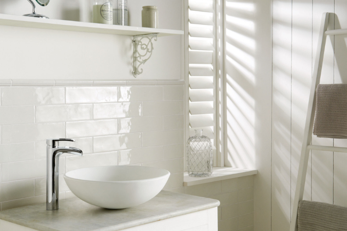 Helles Badezimmer mit rundem weißen Aufsatzwaschbecken, Chromarmatur, gefliestem Hintergrund und dekorativen Accessoires auf Regal
